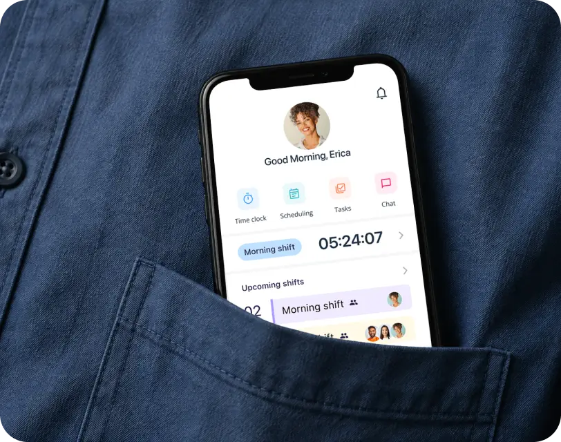 Phone in a shirt pocket displaying a workforce app with time clock, scheduling, and shift details.