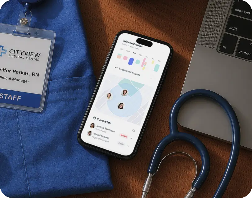 Phone displaying a staff scheduling app next to a stethoscope, nurse badge, and laptop.