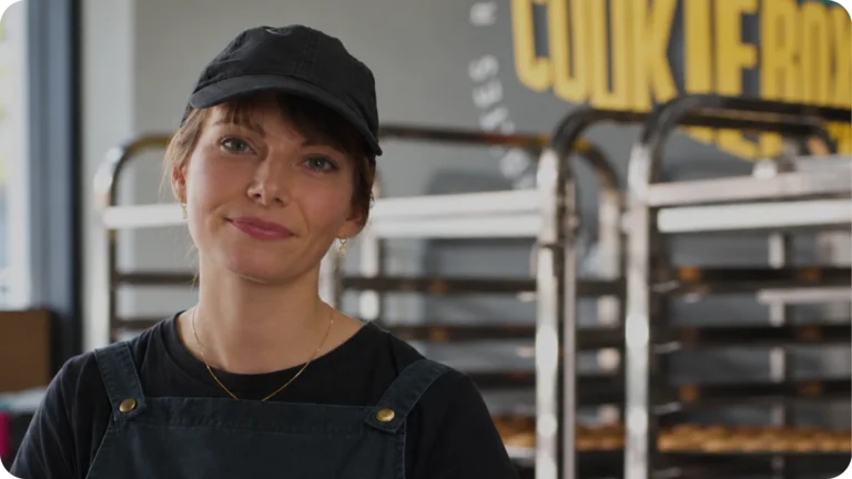 Video thumbnail featuring a smiling employee in a cap and apron inside a Cookie Box bakery.