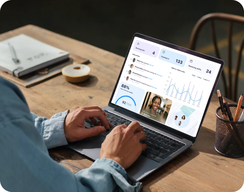 Hands typing on a laptop displaying Connecteam's management dashboard in an office setting.