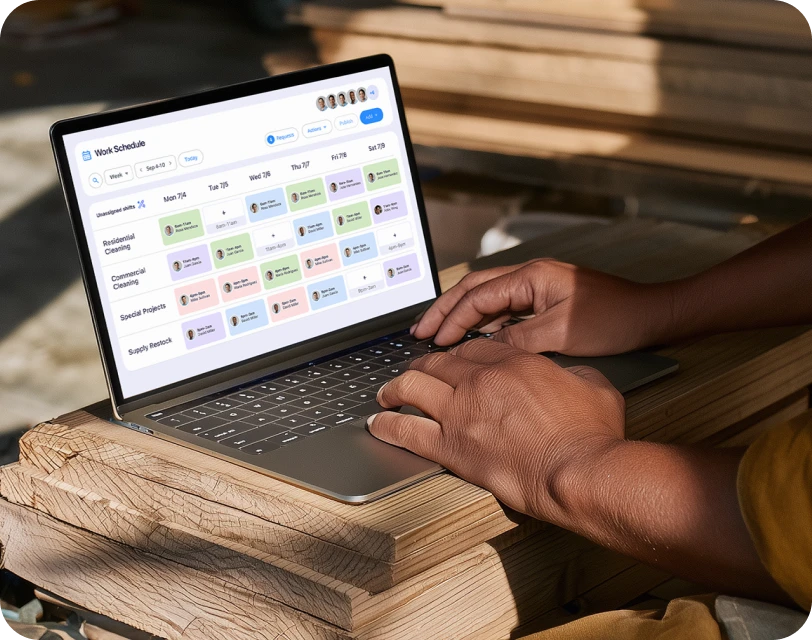 Hands typing on a laptop displaying Connecteam's work schedule dashboard in a construction setting.